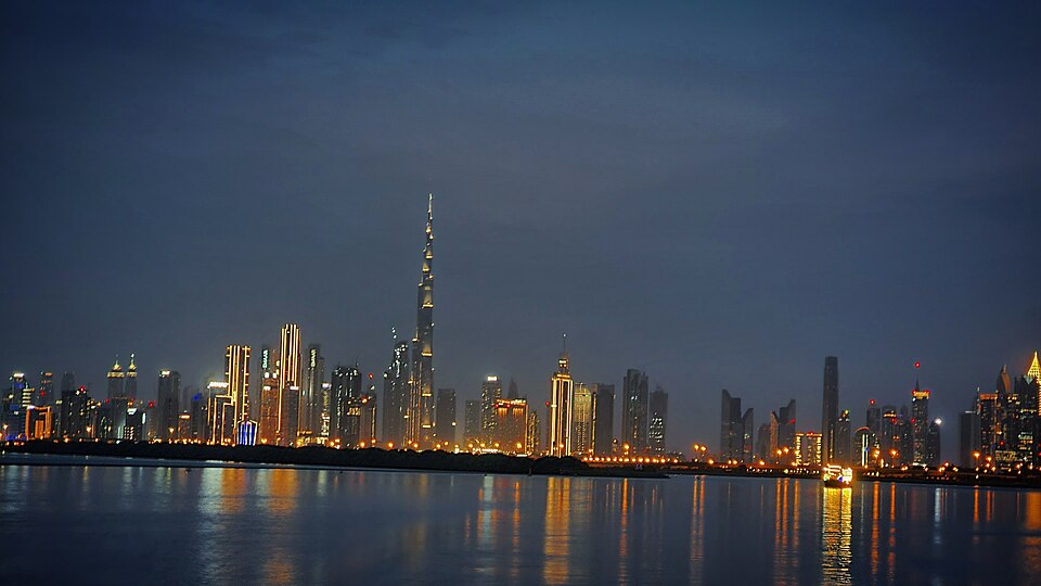 The Burj Khalifa and the towers of Downtown Dubai lit up at night, seen across the water from the Dubai Creek side