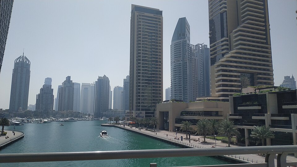 Residential towers along the Dubai Marina canal, with a motorboat on the water and palm-lined promenades on both banks